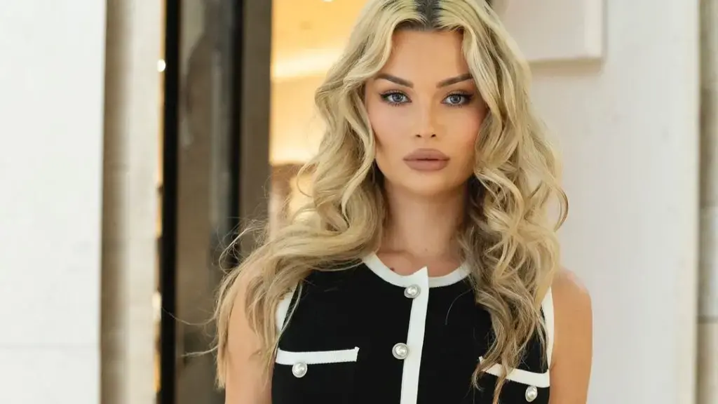 Blerta Veseli e veshur me këmishë të mëndafshtë dhe syze dielli, duke pozuar në një restorant luksoz me stil elegant dhe modern.